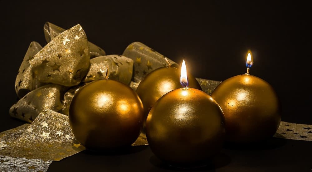 Golden advent candles glowing softly. Four round gold candles with glittery ribbon on dark background