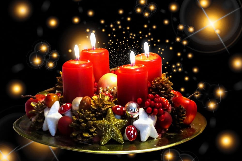 Advent wreath aglow with candles. Four lit red candles on a wreath with pinecones, berries and stars against a dark sparkling background