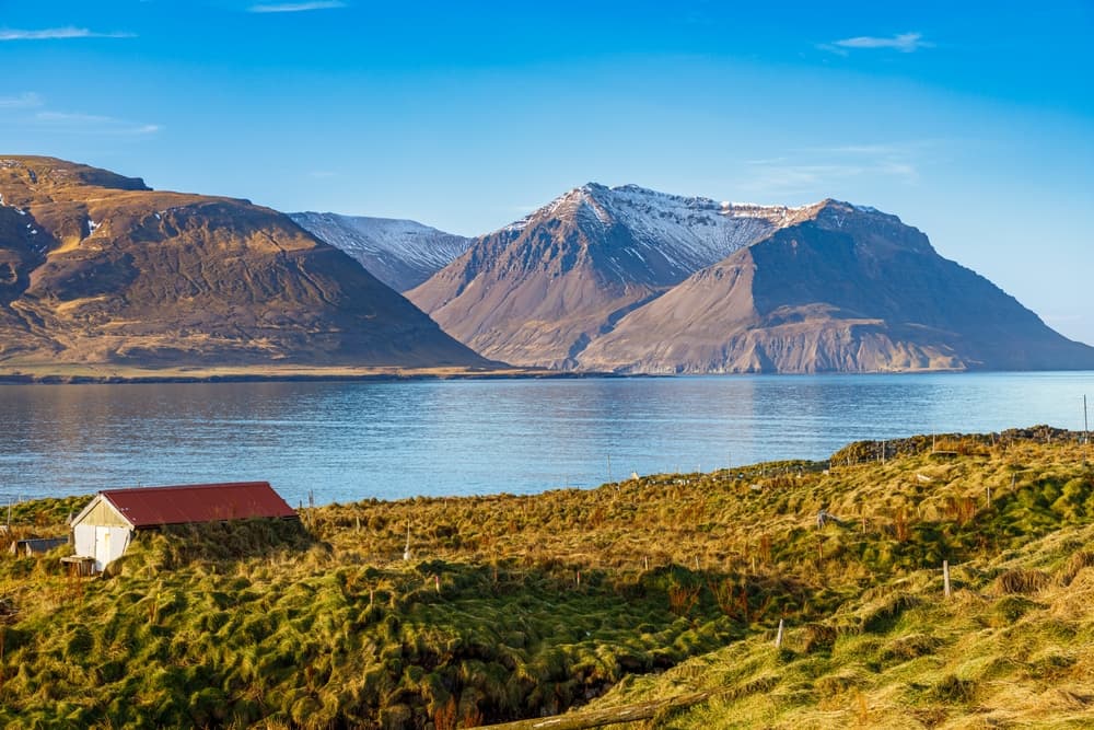 Borgarfjörður Eystri (East Fjords) Serene view of coastal mountains and a small cottage in Iceland’s Eastfjords region on a clear blue morning.