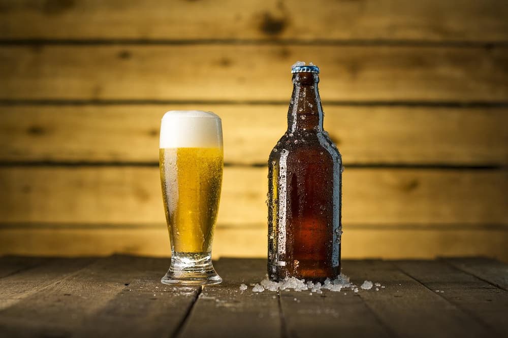 A cold glass of beer. Glass and bottle of beer on a wooden table