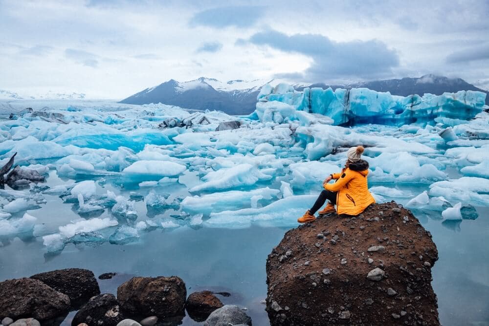 Jökulsárlón, glacier lagoon. Person in yellow jacket sitting on a cliff next to Jökulsárlón, glacier lagoon.