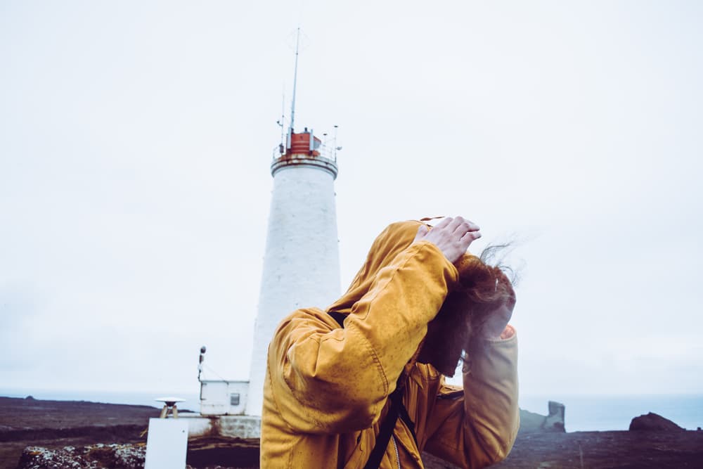 Traveler fighting a storm in Iceland near a lighthouse.