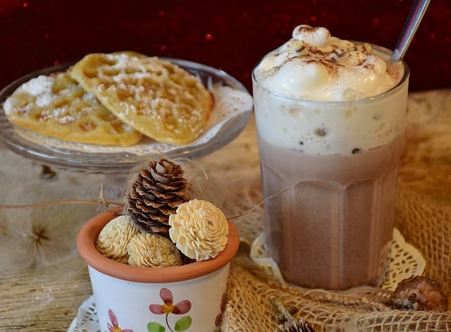 Waffles and iced coffee treat. Waffles with powdered sugar beside a cream topped iced coffee drink