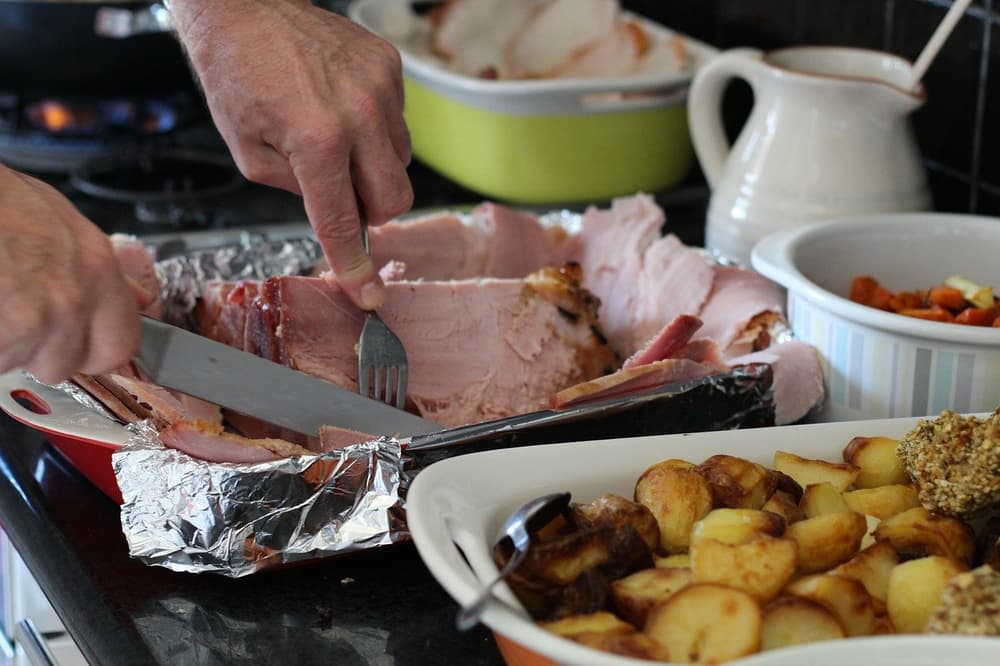 Carving the festive ham. Hands carving sliced ham beside roast potatoes on a kitchen counter