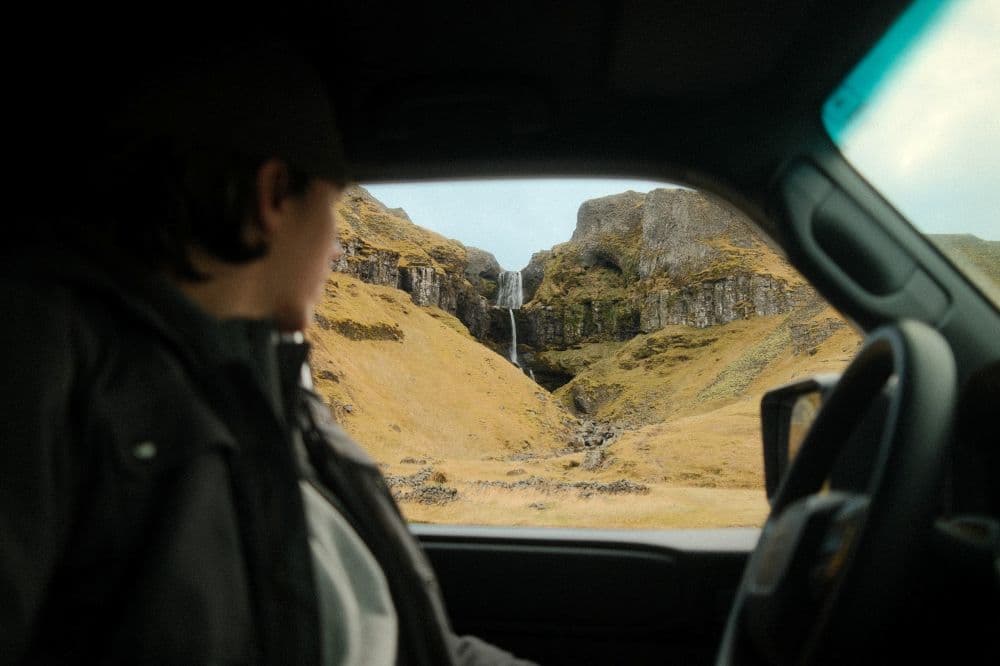 Island Wasserfall Mietwagen. Fahrt in Island mit Blick auf einen Wasserfall aus dem Mietwagen.