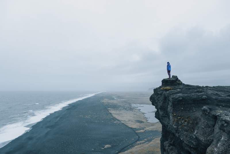 Black sand beach iceland Man standing on cliff at black sand beach iceland