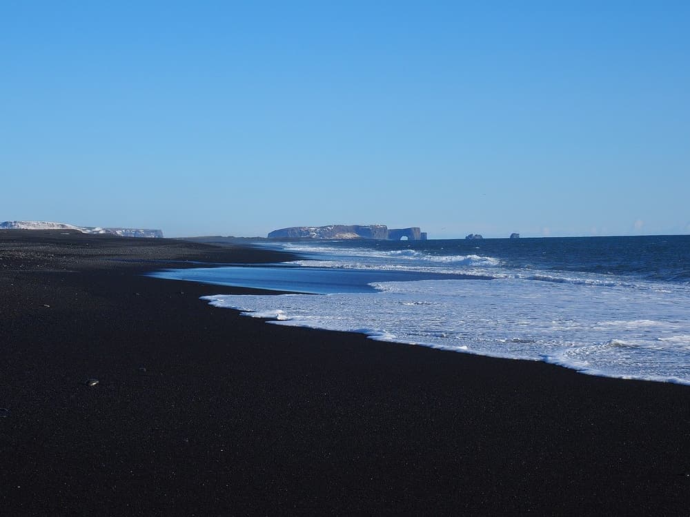 Waves along a black beach. Black sand beach with sea foam and distant cliffs at Dyrhólaey