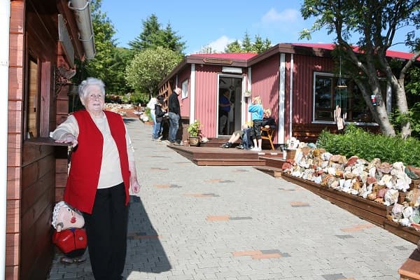 Woman in red vest standing outside red cabin shop in east Iceland