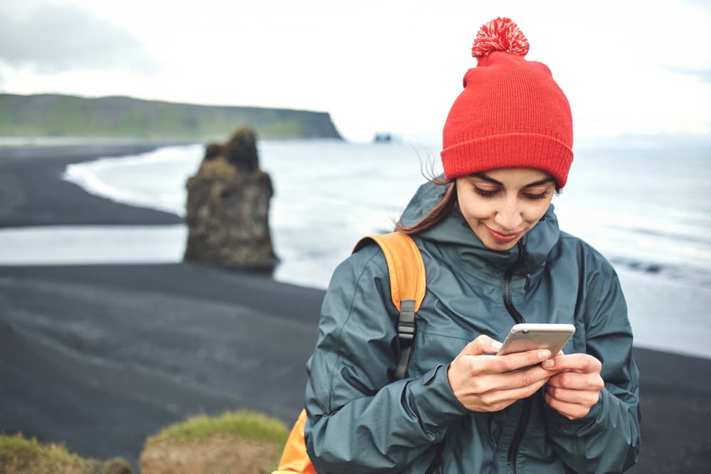 Dyrhólaey und Reynisfjara. Frauen nutzen ein Smartphone bei Dyrhólaey mit Reynisfjara im Hintergrund.