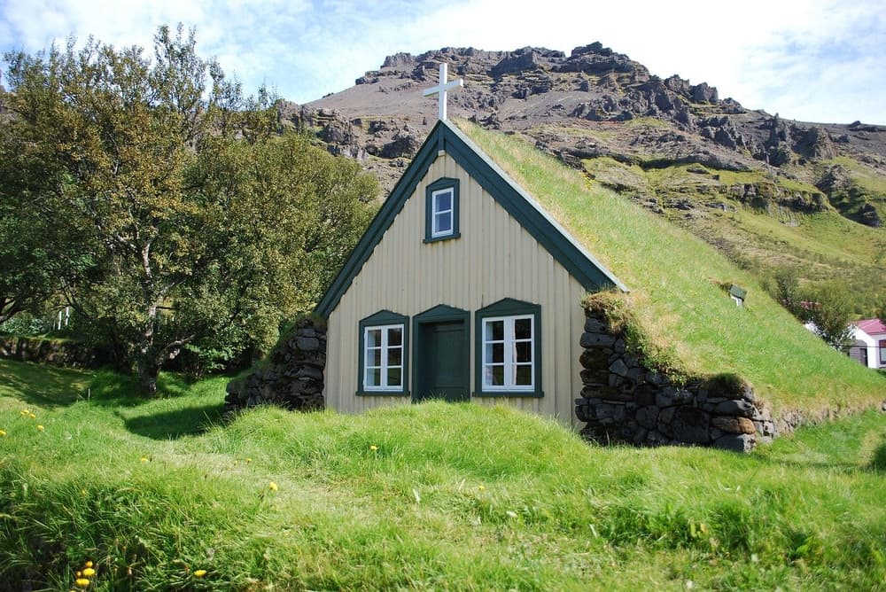 Hofskirkja church and hillside. Turf roofed Hofskirkja church with white cross below a rocky hillside