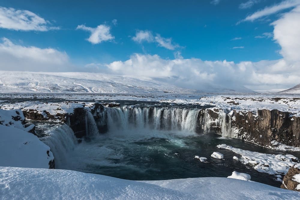 Waterfall in a snowy landscape. Wide waterfall cascading over dark cliffs into a river amid snowy landscape