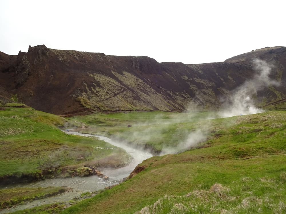 Dampf über einem heißen Quellental. Dampf steigt aus einem Fluss auf, der sich durch ein moosbewachsenes heißes Quellental in Island schlängelt