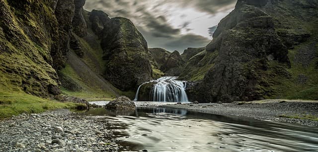 Waterfall in the gorge. Waterfall cascading through a mossy rocky gorge into a shallow river