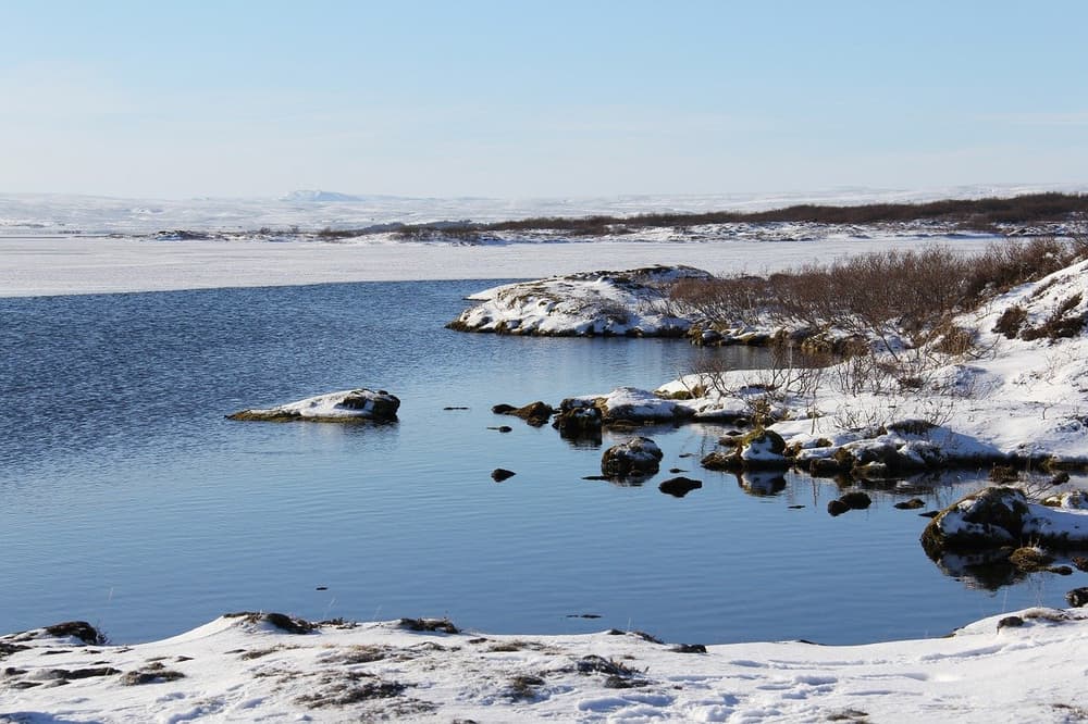 Snow covered rocks along the edge of a calm blue lake