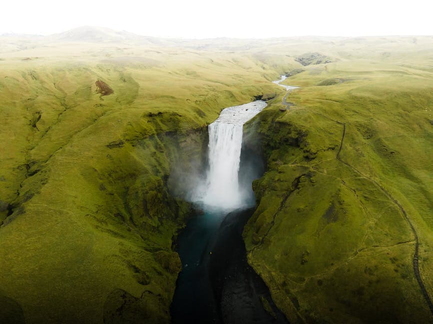 Aerial view of a waterfall dropping through a green canyon