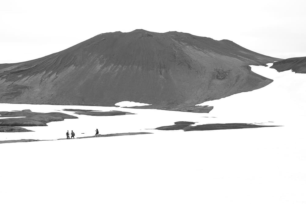 Hiking beneath a snowy peak. Hikers walking across a snowy plain below a large dark volcanic mountain in Iceland