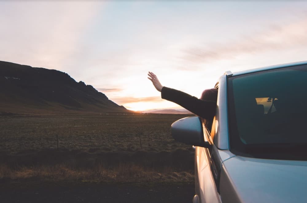 Waving to the sunset. Person leaning out of a car window raising an arm toward a sunset