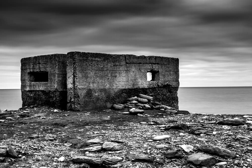 Old pillbox by the sea. Concrete world war two pillbox on a rocky shoreline under cloudy sky, black and white