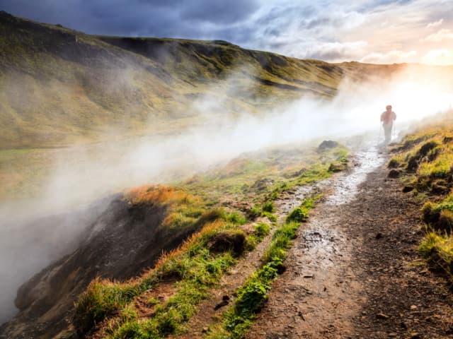 Hiker walking a steaming trail through Reykjadalur valley