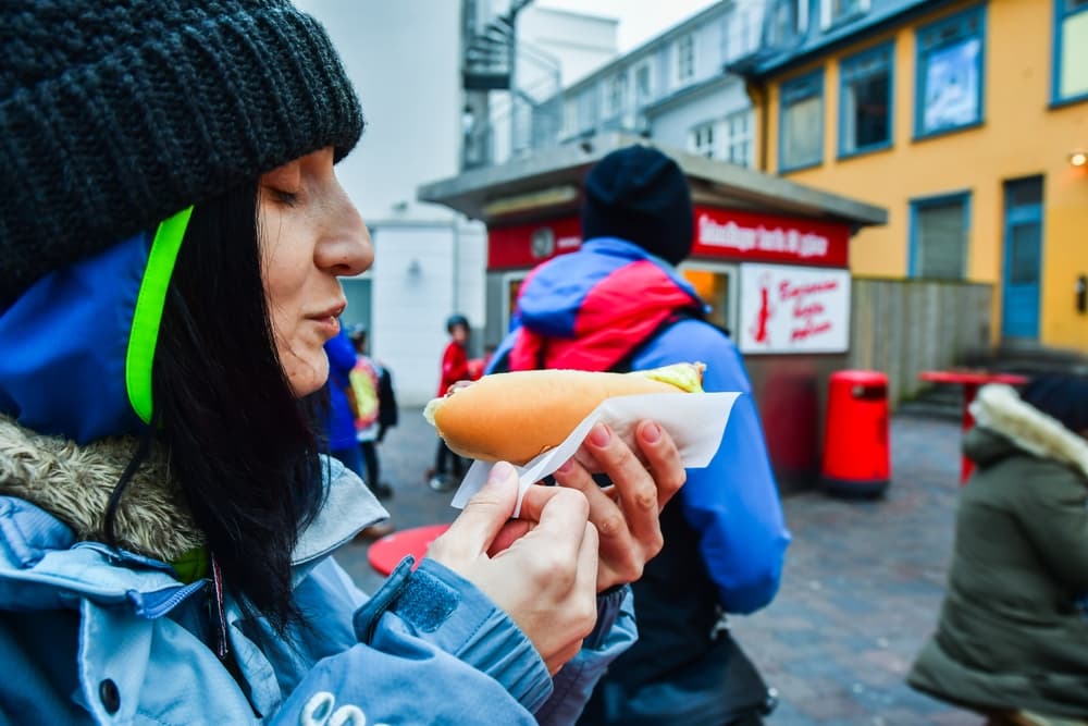 Femme mangeant un hot-dog traditionnel dans un stand célèbre de Reykjavik.