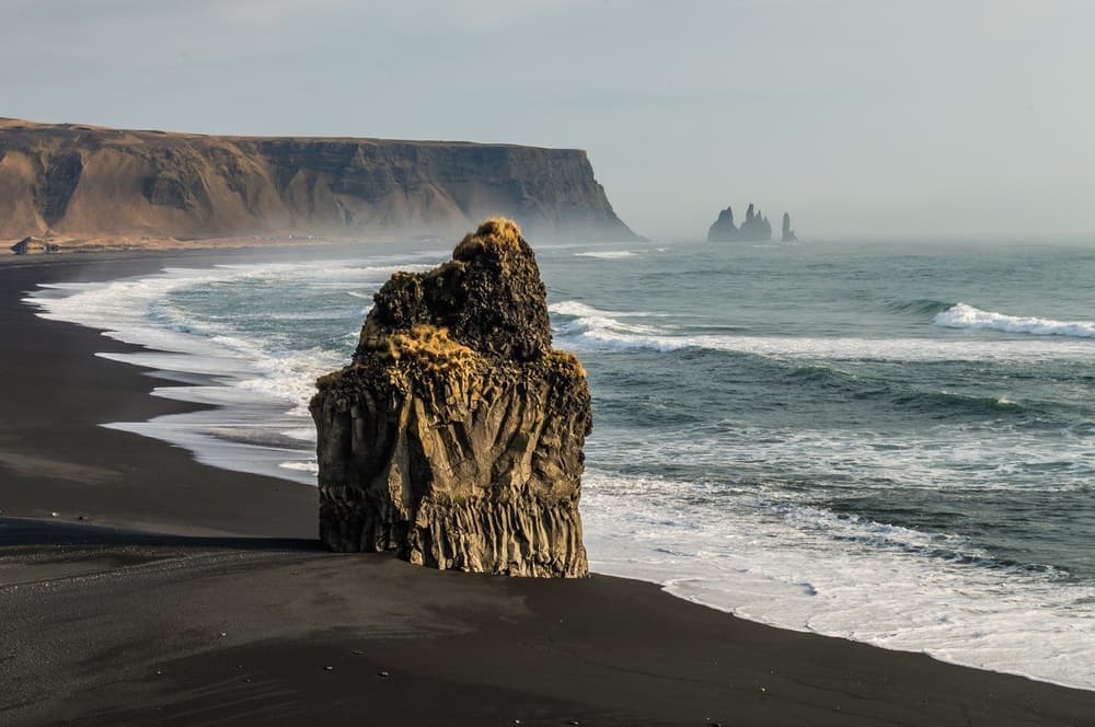 Basalt sea stack at Reynisfjara. Jagged black rock formation on the dark sand of Reynisfjara beach
