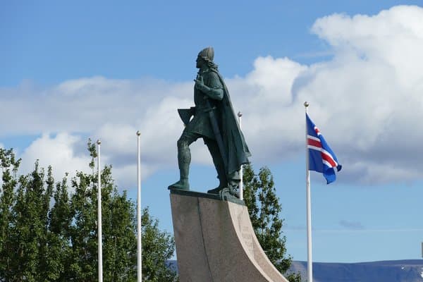A viking statue against the sky. Bronze viking statue on stone plinth with flagpoles and mountains behind