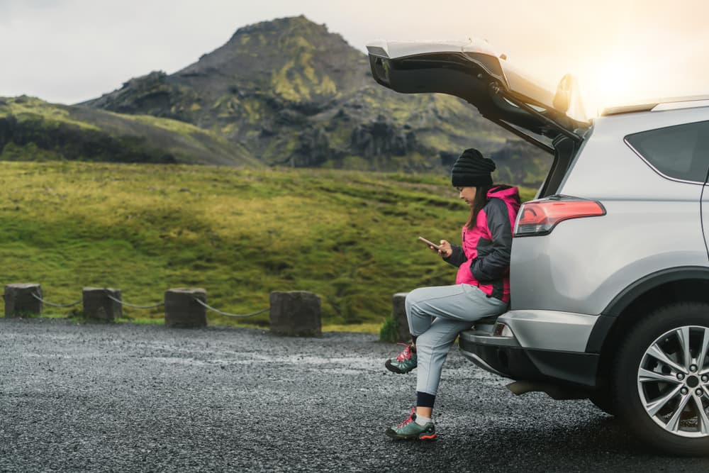 Woman sitting on the trunk of a rental car in Iceland waiting for assistance.