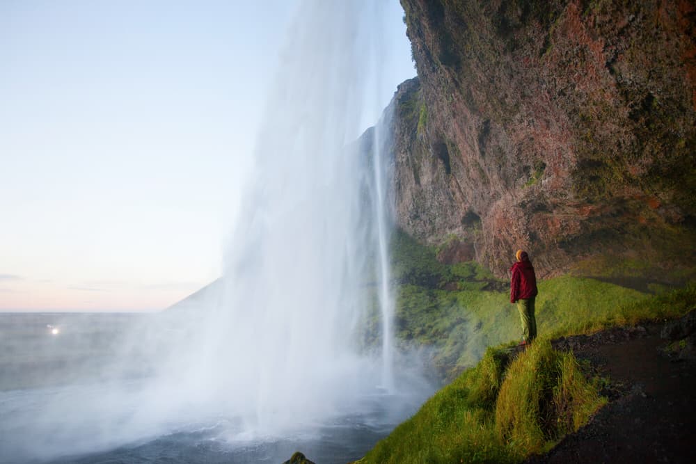Watching Seljalandsfoss up close. Person in red jacket standing near the base of Seljalandsfoss waterfall