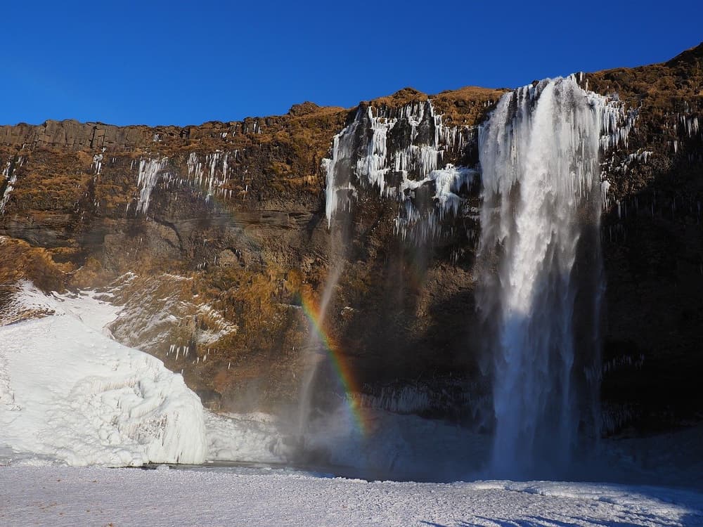 Seljalandsfoss frozen and glowing. Seljalandsfoss waterfall framed by ice, snow and a faint rainbow