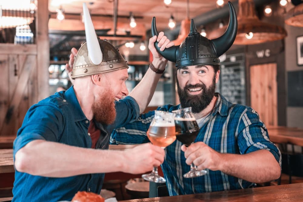 Two men drinking beer at a bar in Reykjavik with Viking helmets. 