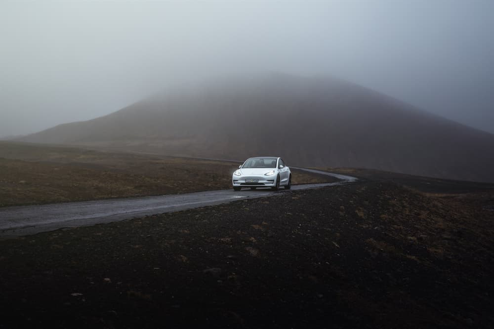 Tesla Blue Car Rental mountain road. Tesla Blue Car Rental Iceland road mountain fog and lava field.