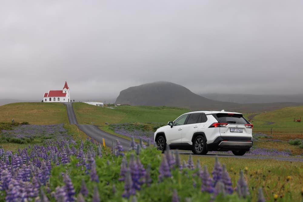 White Toyota Rav4 4x4 on country road with a church in Iceland.