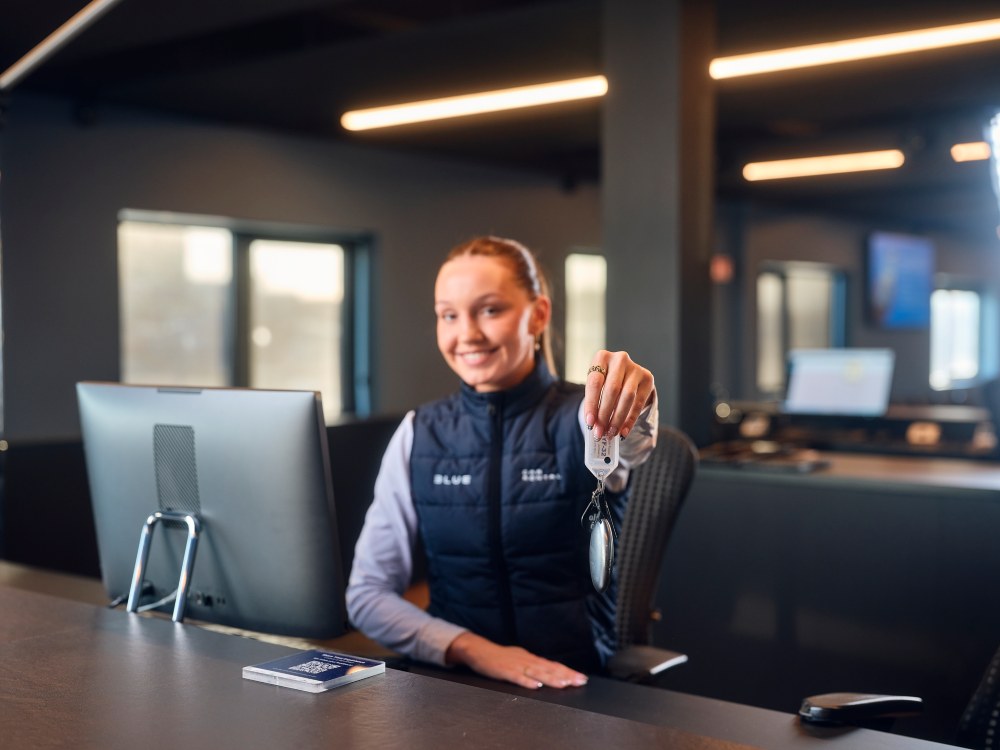 Blue Car rental staff hending over a key to a customer at Kef airport office.