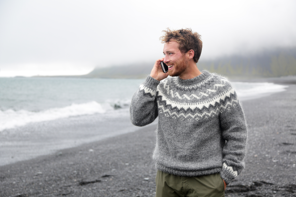 Man in wool sweater on his phone on Iceland black sand beach.