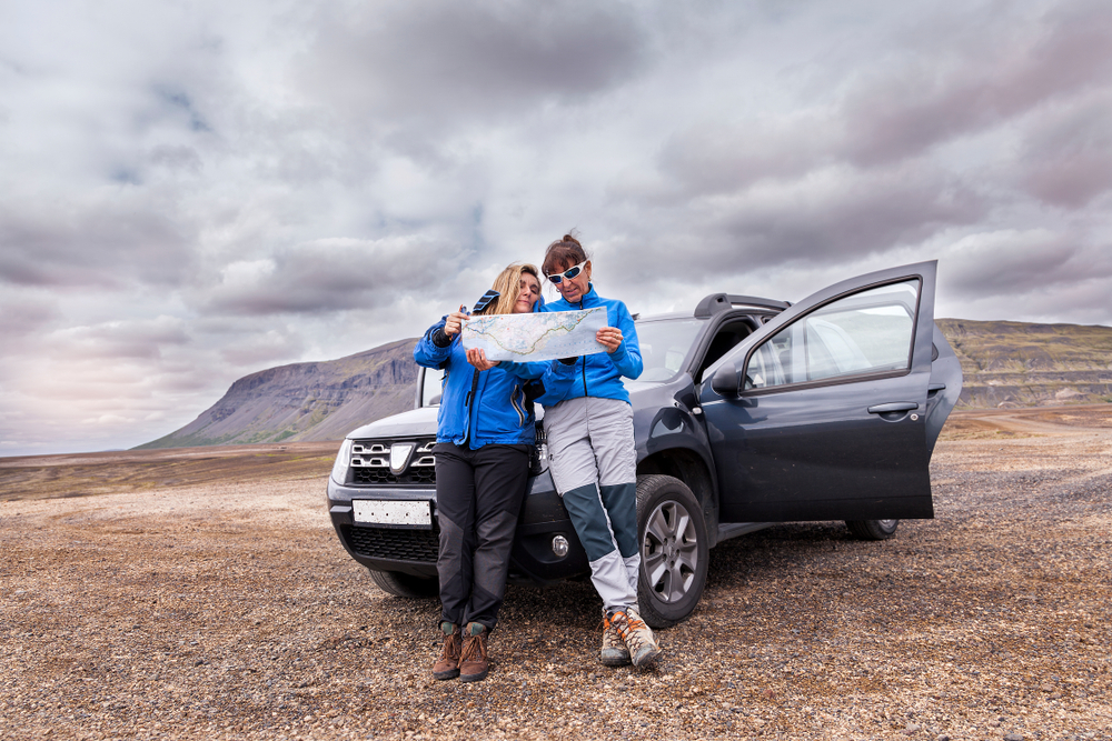 Couple looking at a map in Iceland standing next to a Dacia Duster 4x4.