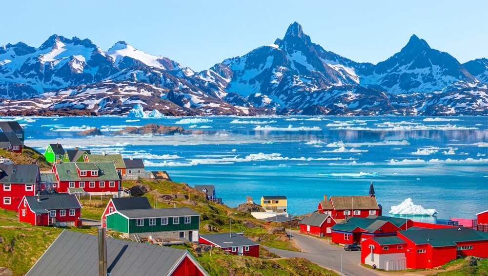 Greenland town with colorful houses and icebergs floating in the blue fjord.
