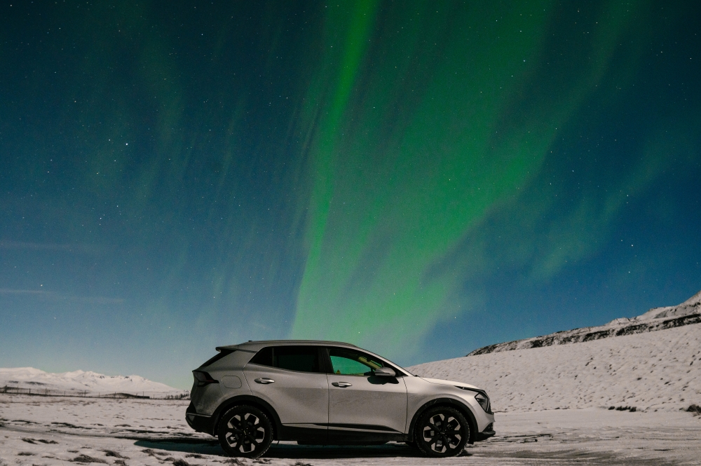 SUV in winter under green northern lights in Iceland.