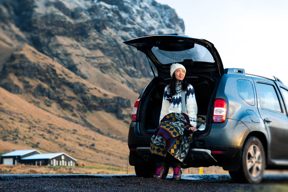 women at vik in iceland sitting on a dacia duster from blue car rental.