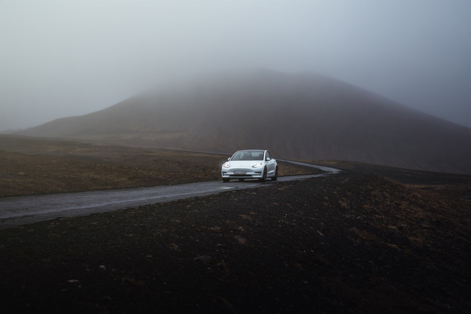 Tesla Blue Car Rental Iceland road mountain fog and lava field.