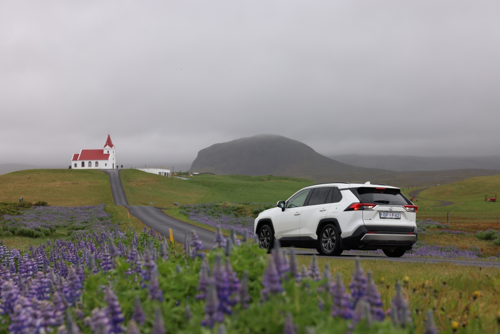 White Toyota Rav4 4x4 on country road with a church in Iceland. 